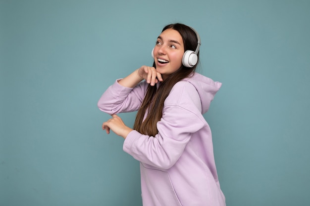 Beautiful happy smiling young brunette female person wearing light purple hoodie isolated over blue background