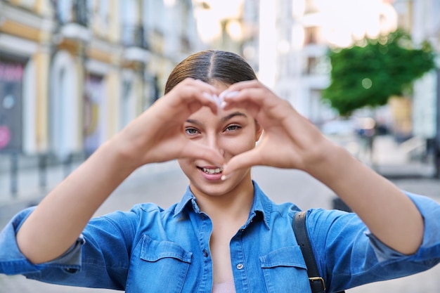 Beautiful happy teenage girl showing heart sign with hands outdoor in the city