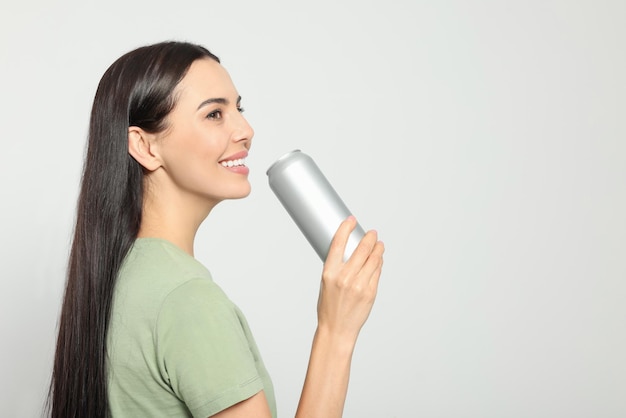 Beautiful happy woman holding beverage can on light grey background Space for text