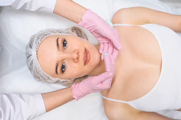 Beautiful happy woman receiving spa treatment cosmetologist in beauty salon with a pink glove