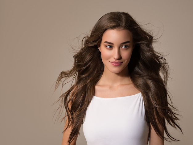 Beautiful happy woman with long hair in white dress over color brown background.Young model portrait