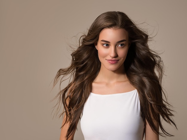 Beautiful happy woman with long hair in white dress over color brown background.Young model portrait