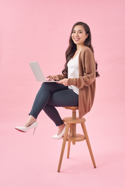 Beautiful and happy woman working with a laptop, isolated over pink background