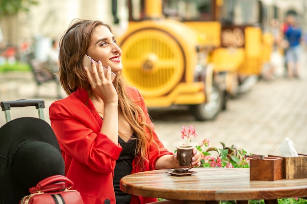 Beautiful happy young caucasian woman talking by cell phone sitting in outdoors cafe at european city