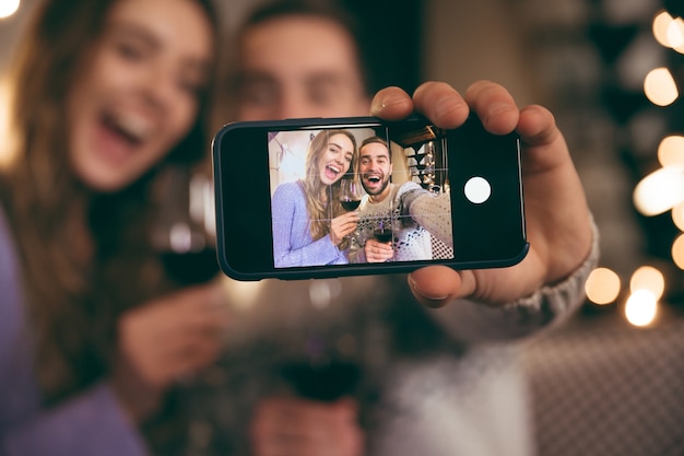 Beautiful happy young couple spending romantic evening together at home, drinking red wine, taking a selfie