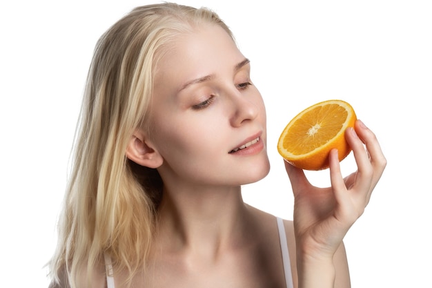 Beautiful happy young sportswoman smelling orange over white wall.