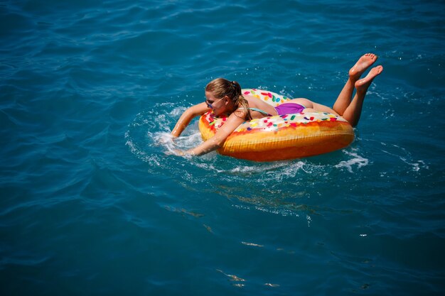 Beautiful happy young woman in a swimsuit with an inflatable ring relaxing in the blue sea. Sunny day, seaside vacation, tourism