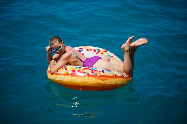 Beautiful happy young woman in a swimsuit with an inflatable ring relaxing in the blue sea. Sunny day, seaside vacation, tourism