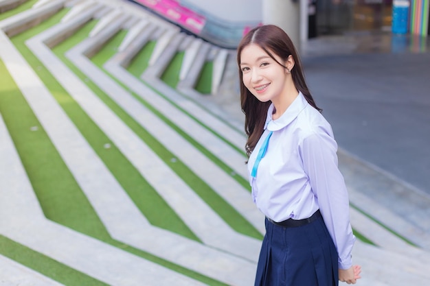 Beautiful high school Asian student girl in the school uniform stands and smiles happily.