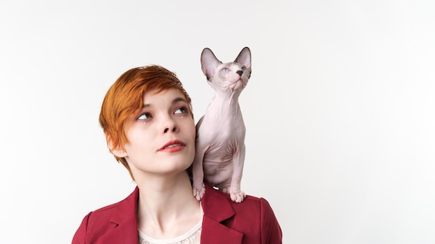 Beautiful hipster redhead young woman looking up and playful Sphynx kitten sitting on her shoulder