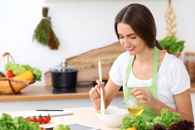 Beautiful  Hispanic woman is cooking in the kitchen. Housewife is tasting fresh salad while sitting at the table