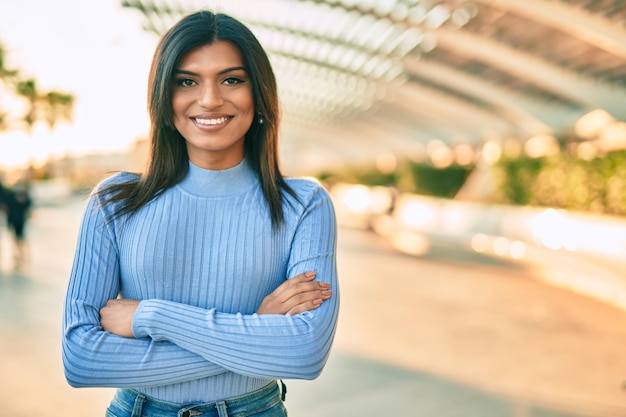 Beautiful hispanic woman smiling confient with crossed arms at the city