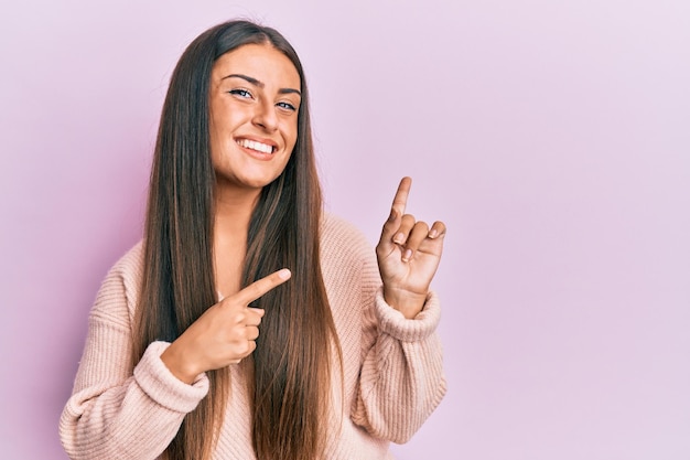 Beautiful hispanic woman wearing casual clothes smiling and looking at the camera pointing with two hands and fingers to the side.