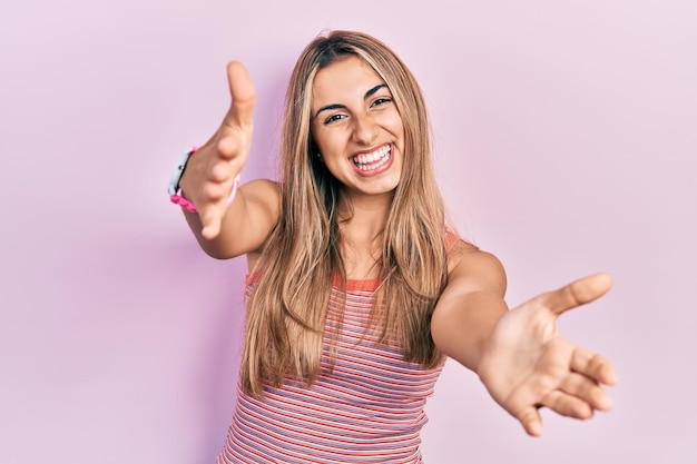 Beautiful hispanic woman wearing casual summer t shirt looking at the camera smiling with open arms for hug. cheerful expression embracing happiness.