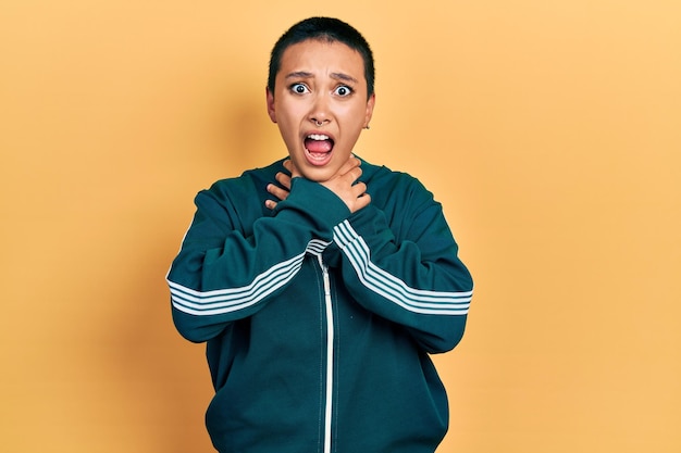 Beautiful hispanic woman with short hair wearing sporty jacket shouting and suffocate because painful strangle. health problem. asphyxiate and suicide concept.