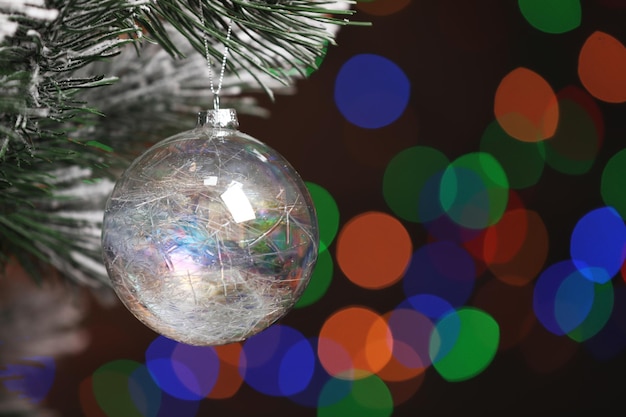 Beautiful holiday bauble hanging on Christmas tree against blurred festive lights closeup Space for text