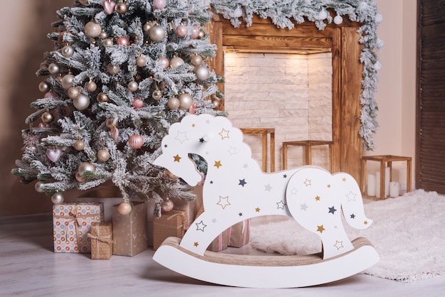 Beautiful holiday decorated room with Christmas tree, wooden horse and presents near the fireplace.