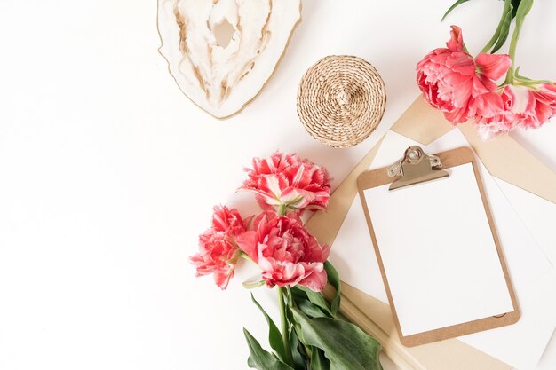 Beautiful home office table desk workspace with fresh pink peony tulip flowers, marble tray, rattan casket, albums. Flat lay, top view