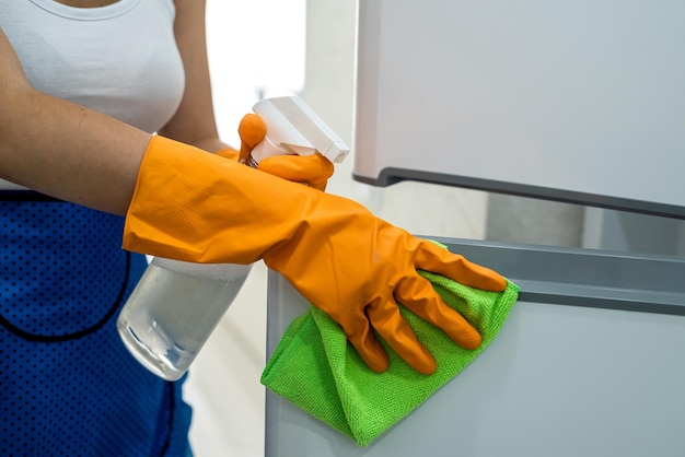 Beautiful housekeeper cleaning refrigerator doors with rag