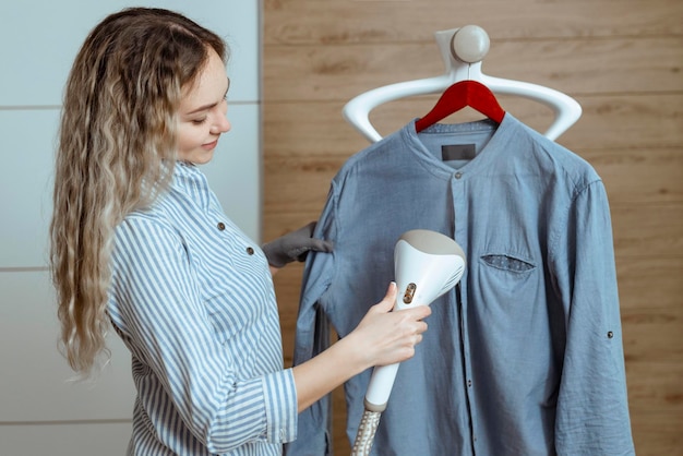 Photo beautiful housewife irons her shirt inside the house with a steamer laundry and dry cleaning