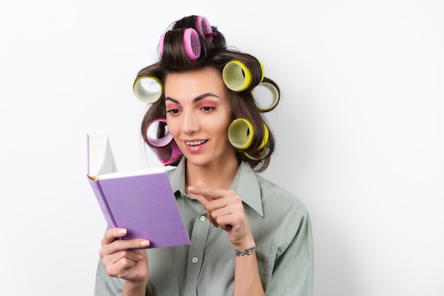 Beautiful housewife Young cheerful woman with curlers bright makeup with a book in her hands on a white background Thinking about a dinner recipe Looking for food ideas