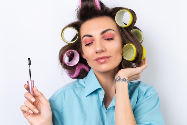 Beautiful housewife A young cheerful woman with hair curlers bright pink makeup and mascara is preparing for a date night dinner on a white background