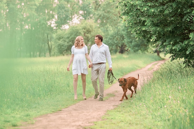 Beautiful husband and his pregnant wife with their dog on a walk in the Park