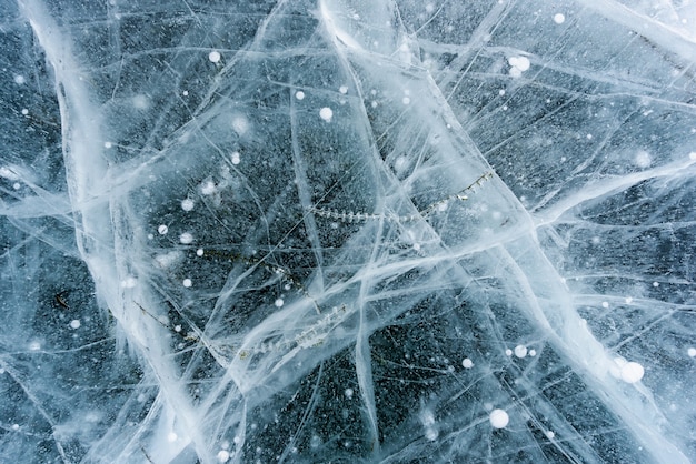 Beautiful ice of Lake Baikal with abstract cracks and green plant in the deep