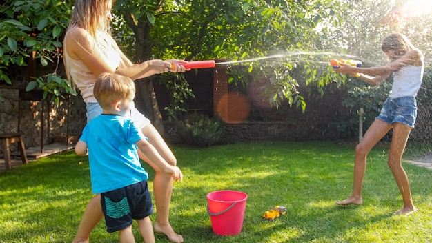 Beautiful image of happy laughing family with children having fun at hot summer day with water guns and garden hose. Family playing and having fun outdoors at summer