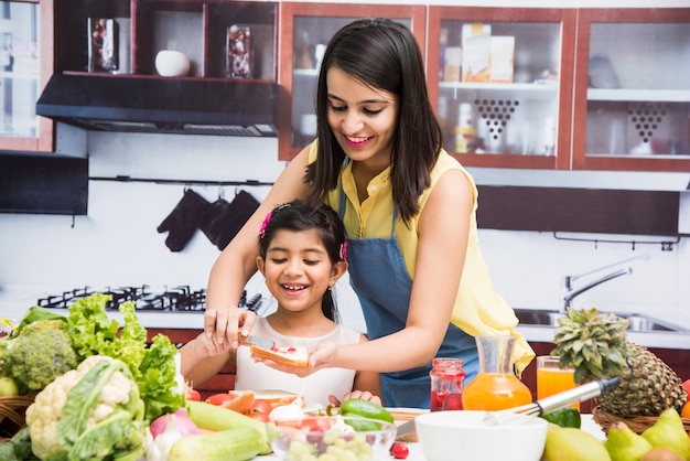 Beautiful Indian or Asian young Mother and Daughter in kitchen, with table full of fruits and vegetables