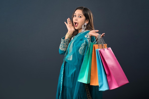 Beautiful Indian young girl holding and posing with shopping bags on a grey background