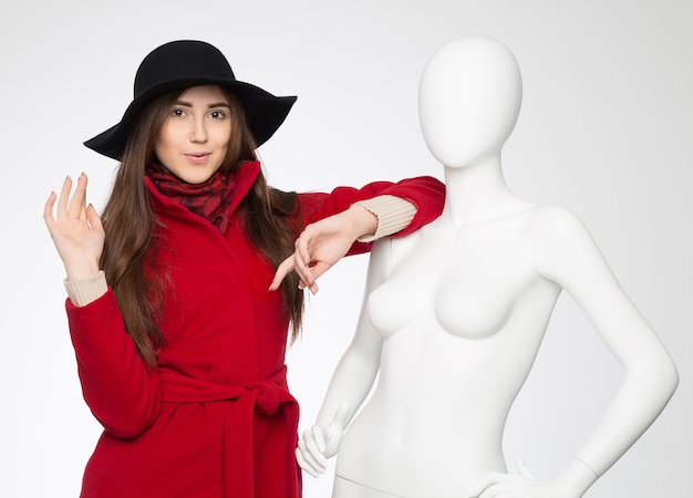 Beautiful interesting girl in the hat next to the white female mannequin on grey background