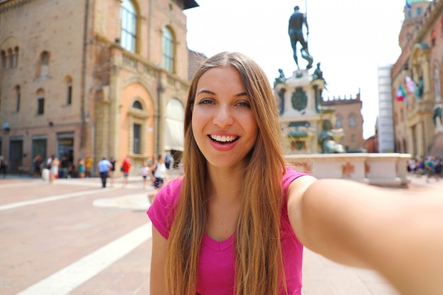 Beautiful Italy. Attractive smiling young woman take self portrait in Piazza del Nettuno square Bologna city, Italy.