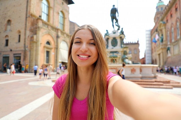 Beautiful Italy. Attractive smiling young woman take self portrait in Piazza del Nettuno square Bologna city, Italy.