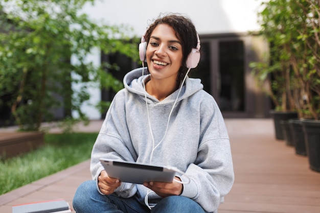 Beautiful lady sitting in headphones with tablet in hands and happily 