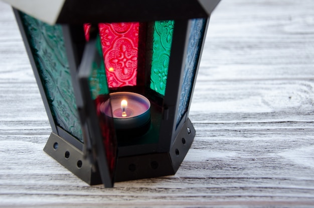 Beautiful lantern with a candle burning inside on a gray wooden background, selective focus on the candle