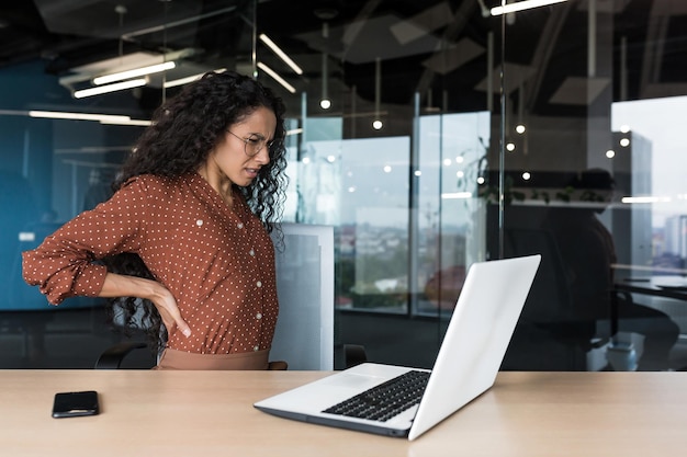 Beautiful latin american businesswoman working in modern office worker overtired has severe back