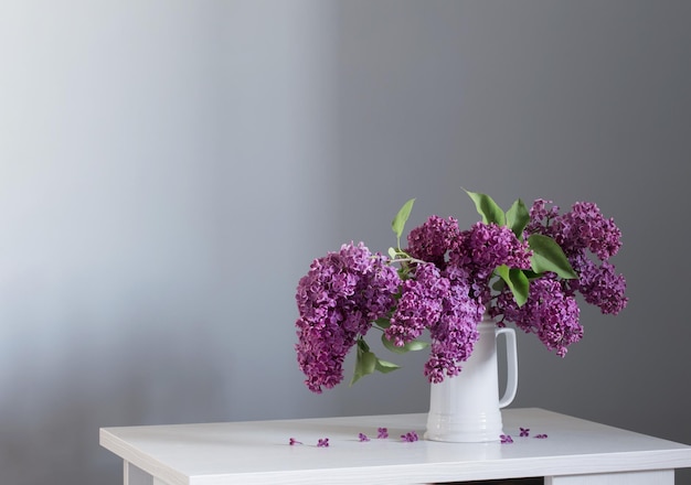 Beautiful lilac flowers in white jug on white wooden table