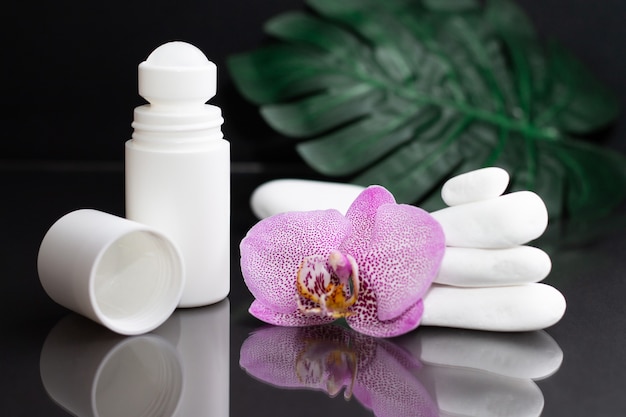 Beautiful lilac orchid flower and white roll-on deodorant with white stones and monstera leaves