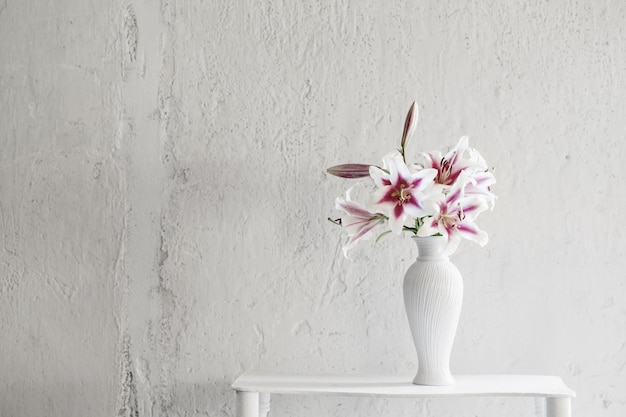 Beautiful lilies in ceramic vase on background white wall