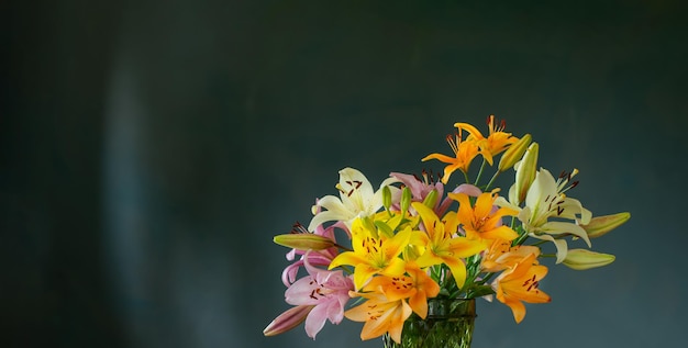 beautiful lilies in glass green vase on dark background