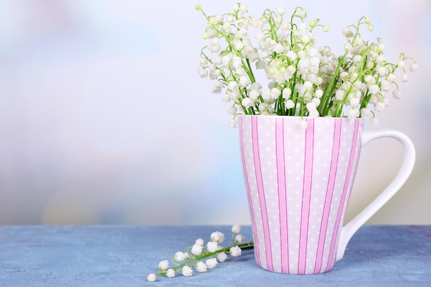 Beautiful lilies of the valley in cup on light background