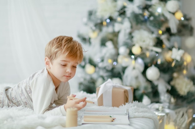 Beautiful little baby boy in pajamas with stars celebrates Christmas. New Year's holidays. Toddler play in white Christmas sleigh in the festively decorated room, copy space on right area.