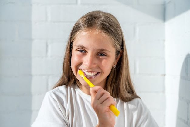 beautiful little baby girl brushing her teeth against the background of a white brick wall