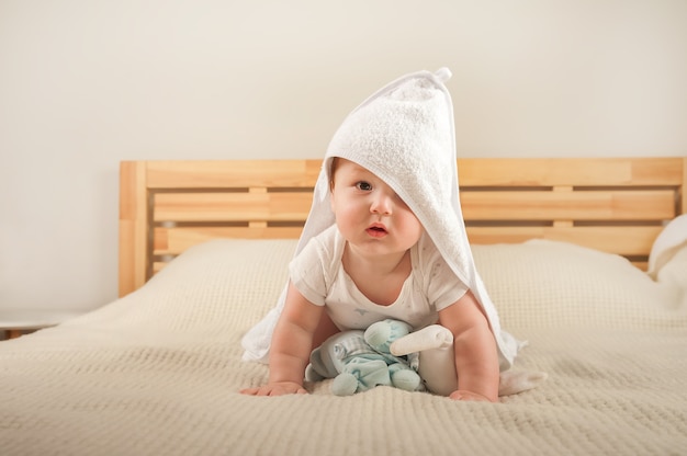 Beautiful little baby in a white towel on the bed close-up and copy space.