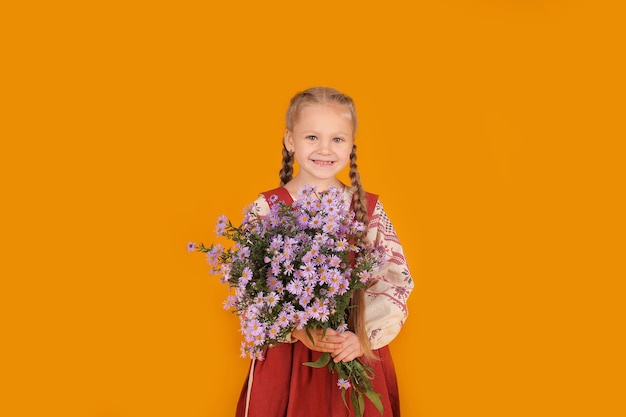 a beautiful little blonde girl in a beige red sundress holds purple flowers in her hands