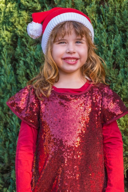 Beautiful little blonde girl posing in Christmas clothes and pine trees background