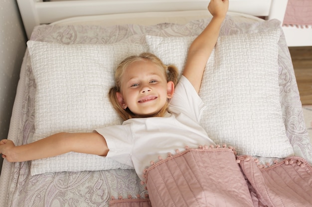 beautiful little blonde girl in a white tshirt sleeps at home under a pink blanket