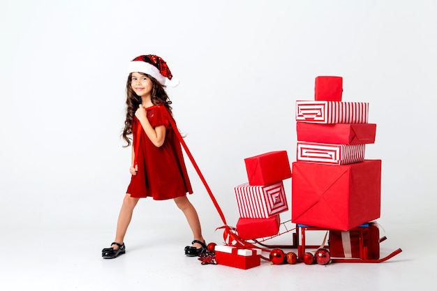 beautiful little brunette girl in a santa costume carries christmas gifts on a sleigh space for tex