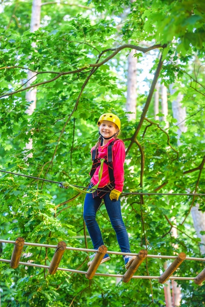 Beautiful little child climbing and having fun in adventure Park Hiking in the rope park girl in safety equipment Kid climbing trees in park Cute child boy